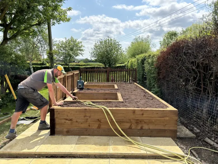 A silver tree services staff member works on a raised flower bed.