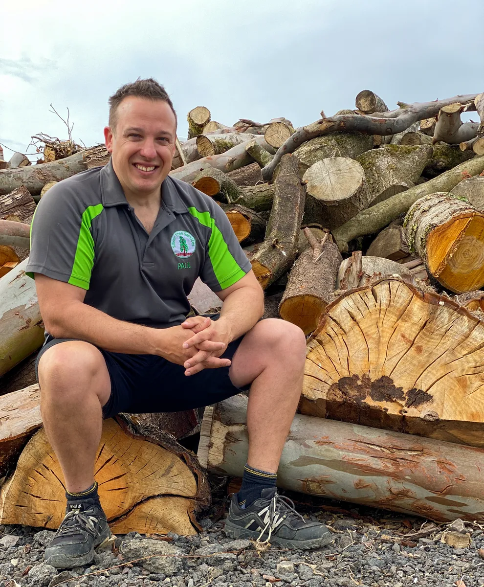 A photo of paul the company founder sitting in front of some logs.