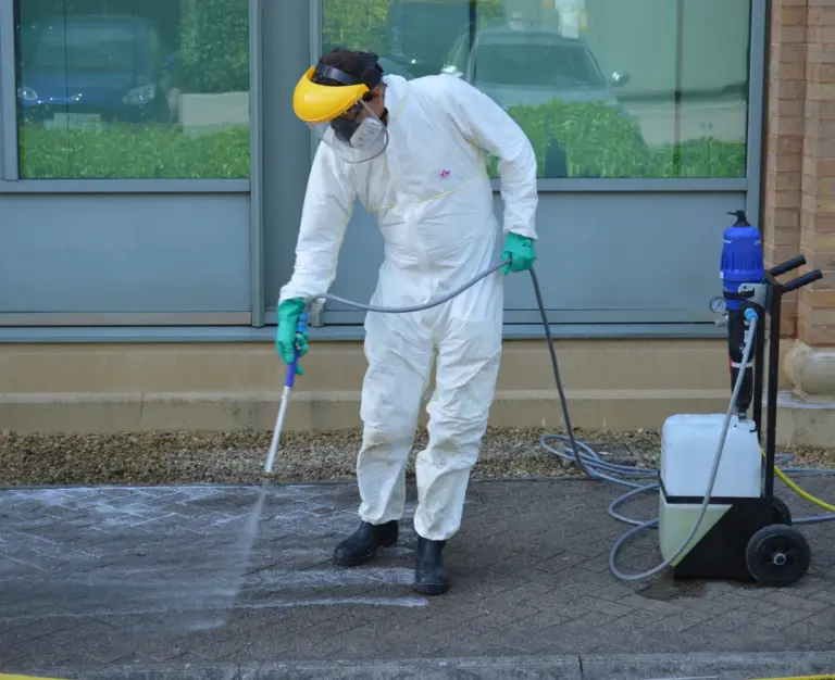 A silver tree services staff member wearing a white protective suit softwashes paving stones and masonary.