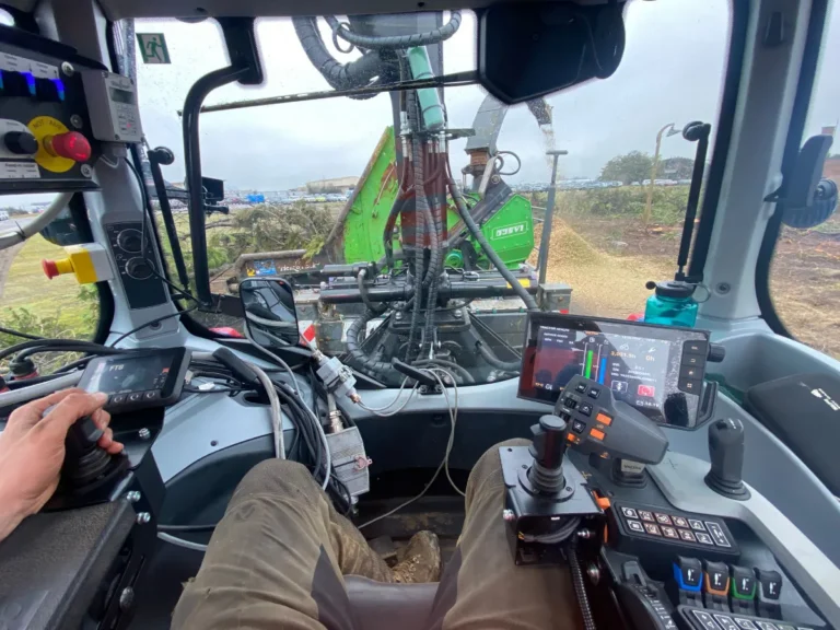 Inside the cabin of a Valtra Tractor feeding logs into a chipper, seen from chest height of operator.