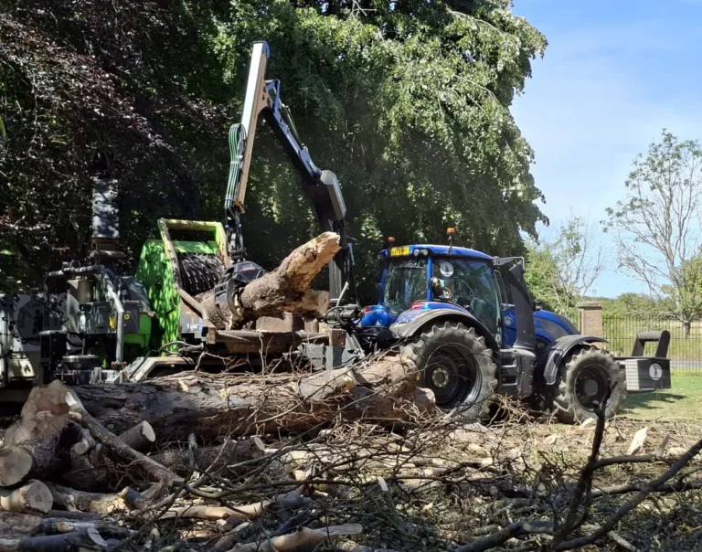 A Valtra Tractor with a crane attachment feeding a wood chipper logs.